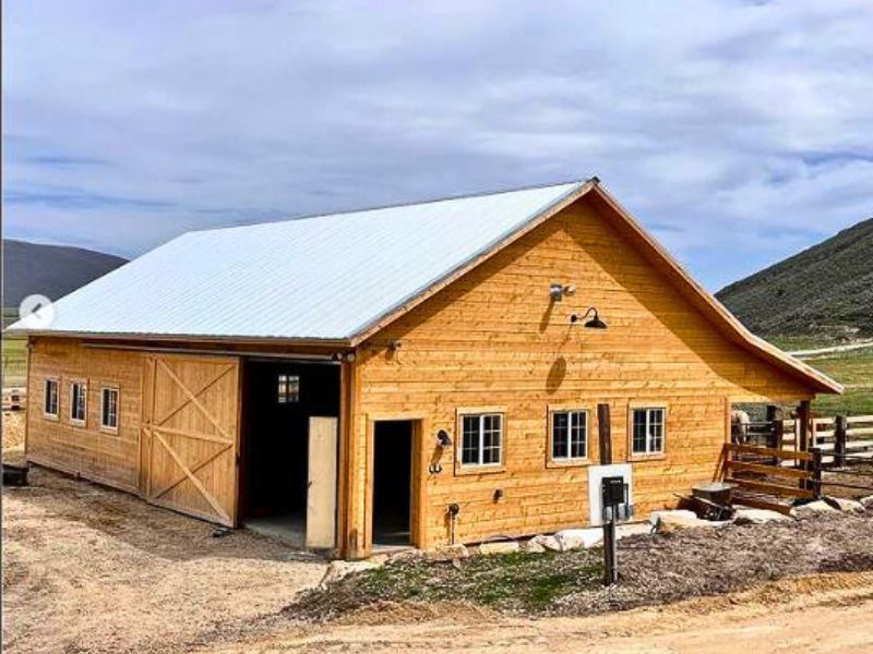  A charming wooden barndominium with a metal roof, barn doors, and a spacious design set in a rural landscape